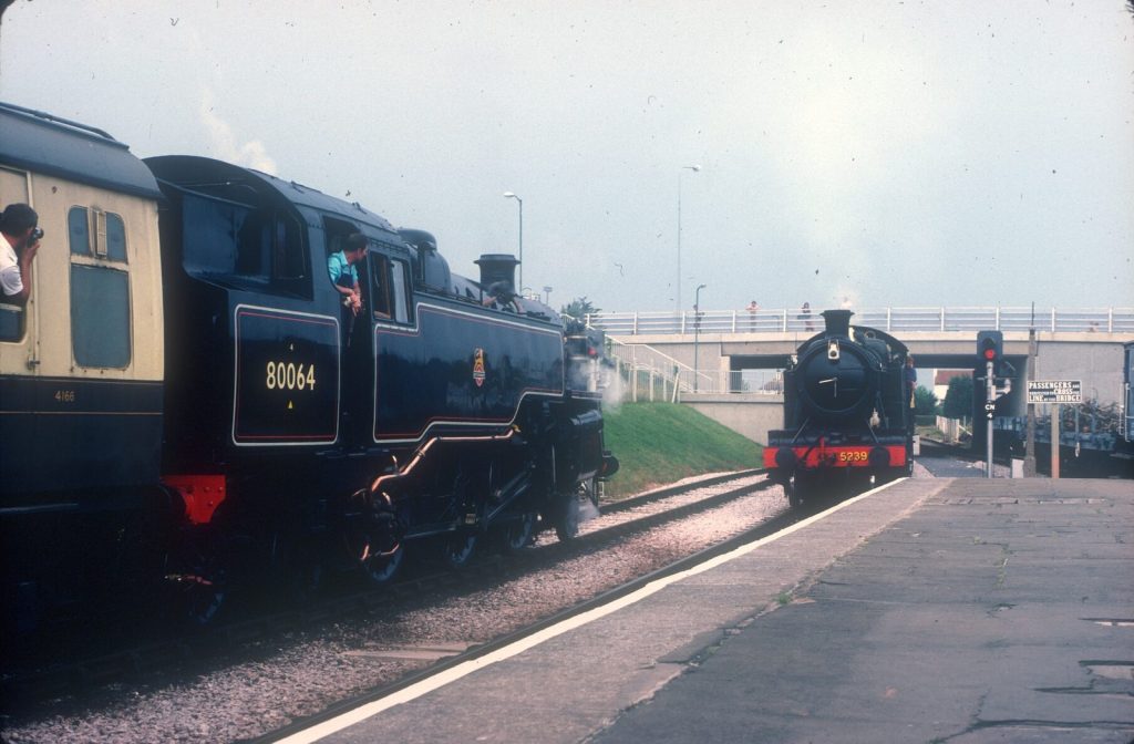 The bunker end of 80064 with the driver leaning out of the cab, as another tank engine, 5239, approaches under a road bridge.