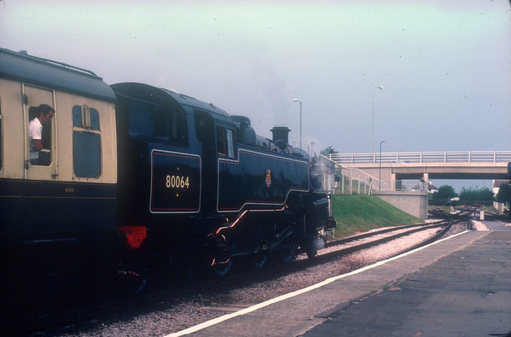 Side view of 80064 coupled to a cream coach, a passenger leaning from the coach window.