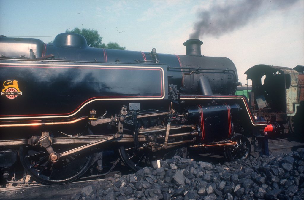 Close view of 80064 beside a coal stack, its British Railways crest and red and cream lining catching the sun.